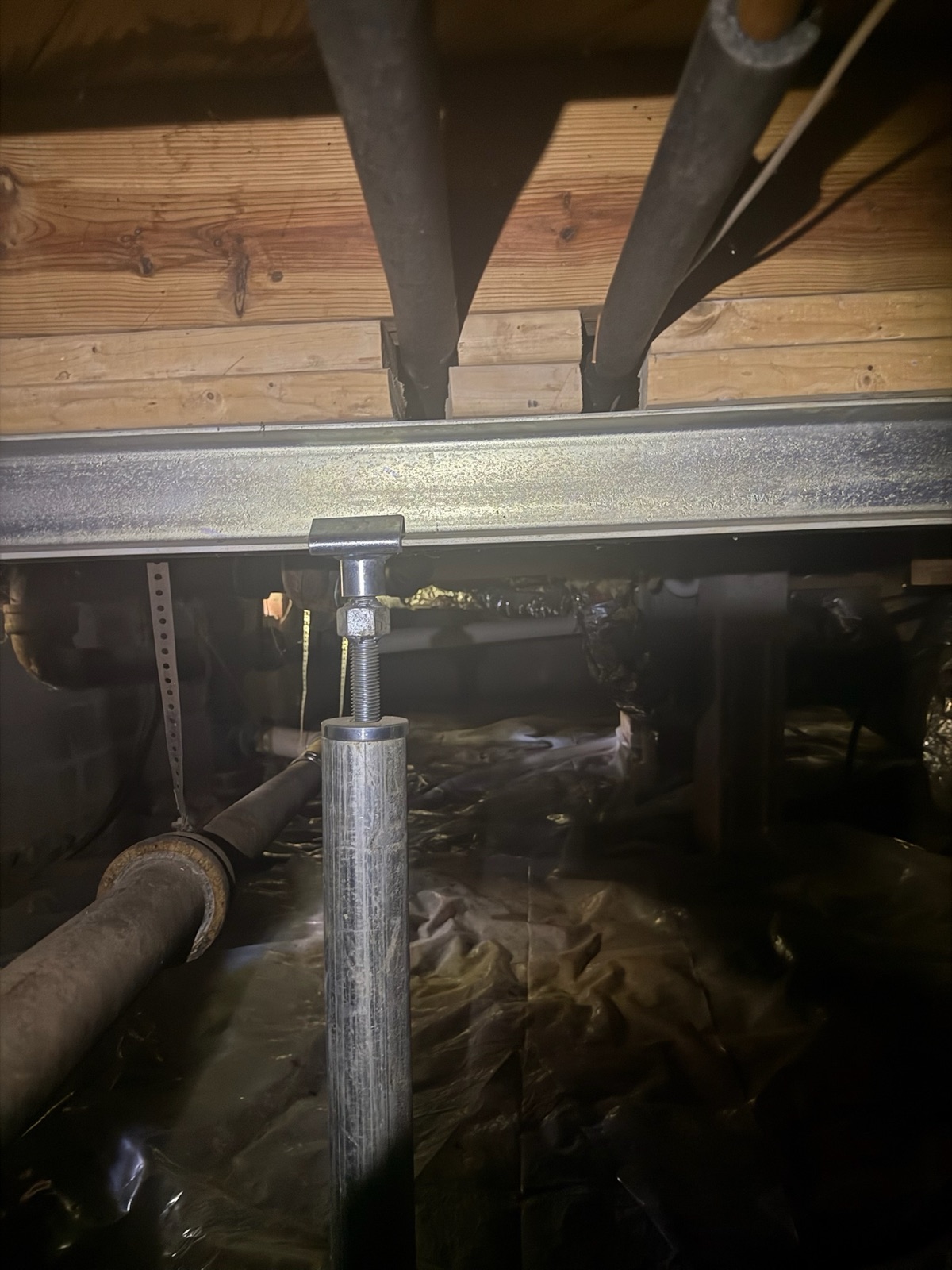 Steel I-beam on an adjustable support jack being installed under floor joists during crawl space repair