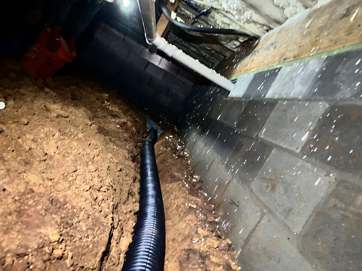 Black perforated drain pipe routed through a block wall to divert water — interior drainage install
